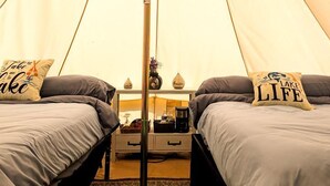 Una carpa con dos camas, un poste central y una pequeña mesa con una lámpara.