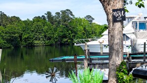 Un lago tranquilo con barcos amarrados, un cartel en un árbol y una planta en maceta.