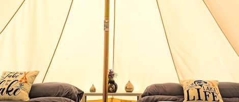 A tent with two beds, a central pole, and a small table with a lamp.
