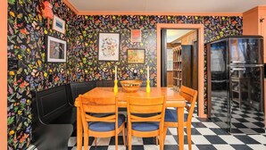 A dining area with a black and white checkered floor, a black wall with colorful floral wallpaper, a black booth seating area, and a black refrigerator. - Cozy cottage with private access to Great Sacandaga Lake. (Hadley)