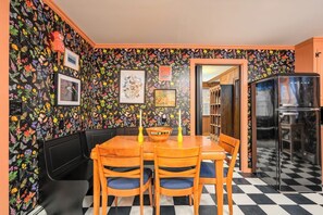 A dining area with a black and white checkered floor, a black wall with colorful floral wallpaper, a black booth seating area, and a black refrigerator.