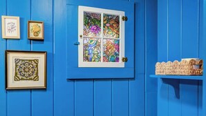 A blue door with a stained glass window, a framed picture, and a woven basket on a blue wall. - Cozy cottage with private access to Great Sacandaga Lake. (Hadley)