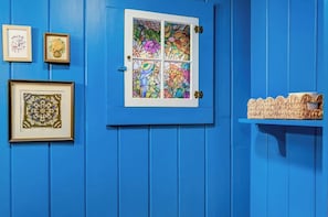 A blue door with a stained glass window, a framed picture, and a woven basket on a blue wall.