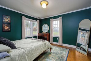 A bedroom with a bed, dresser, mirror, and artwork on the wall.