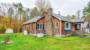 A log cabin with a stone chimney, a porch, and a tent in the yard. - Cozy cottage with private access to Great Sacandaga Lake. (Hadley)