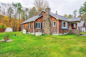 A log cabin with a stone chimney, a porch, and a tent in the yard.