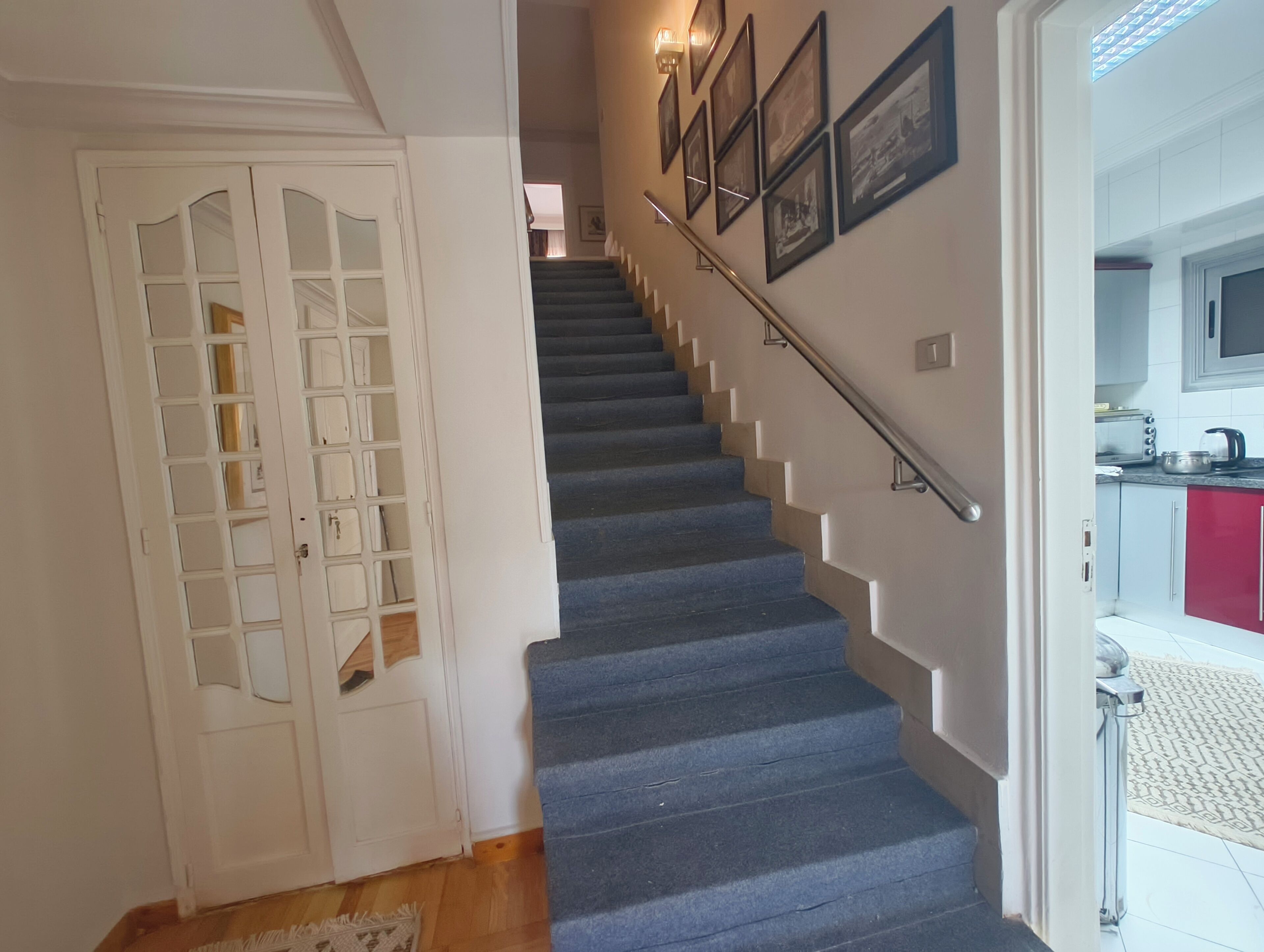 A staircase with a handrail, a white door with glass panels, and a kitchen area with a microwave and toaster.