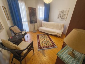Ett vardagsrum med en soffa, en fåtölj, ett litet bord, en golvlampa och en bordsfläkt.