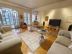 A spacious living room with a large TV, comfortable seating, and a view through a glass door. - Spacious 3-bedroom condo in lovely Giza Governorate with AC and fitness room (Giza Governorate)
