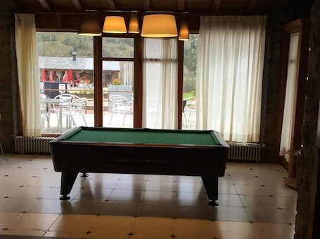 A pool table in a room with large windows, a radiator, and a view of outdoor seating.. HOTEL BON REPOS