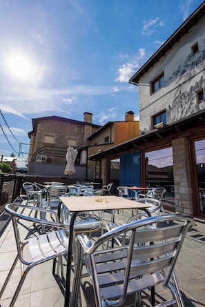 An outdoor seating area with metal chairs and tables, a stone building with a mural, and a clear sky.