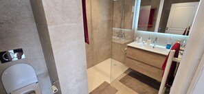 Ein modernes Badezimmer mit Duschkabine aus Glas, einer weißen Toilette und einem hölzernen Waschtisch mit Spiegel.
