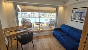 Ett kompakt bostadsutrymme med ett skrivbord i trä, en blå soffa och utsikt över en pool och byggnader.