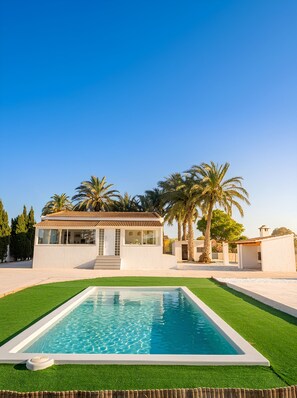 Une maison moderne avec une piscine, des palmiers et un ciel d’un bleu éclatant.