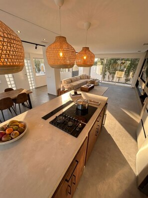 Une cuisine moderne dotée d’un îlot central, de luminaires suspendus et offrant une vue sur l’extérieur.