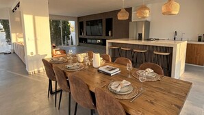 Uma zona de refeições moderna com mesa de madeira, cadeiras estofadas em castanho e iluminação pendente.