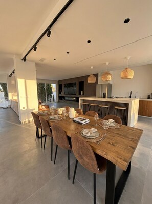 Un espace de salle à manger moderne avec une table en bois, des chaises à revêtement marron et des luminaires suspendus.
