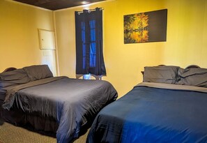 Une chambre avec deux lits, une fenêtre avec des rideaux bleus, un tableau au mur et une porte.