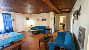 A cozy living room with a wooden ceiling, a blue sofa, a blue armchair, a wooden coffee table, and a small table with a vase.