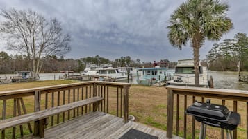 A wooden deck with a grill, overlooking a marina with boats and a small cabin.