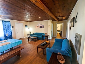 A cozy living room with a wooden ceiling, a blue sofa, a blue armchair, a wooden coffee table, and a small table with a vase. - Lakefront Boathouse with Private Dock & Lake Views in Eutaw Springs, South Carolina (Eutaw Springs)