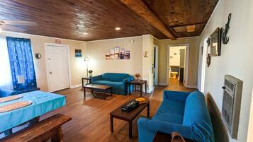 A cozy living room with a wooden ceiling, a blue sofa, a blue armchair, a wooden coffee table, and a small table with a vase.