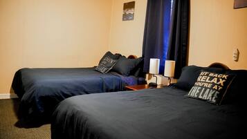 A hotel room with two beds, a nightstand, a lamp, and a window with curtains.