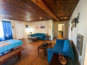 Una sala de estar acogedora con techo de madera, un sofá azul, un sillón azul, una mesa de centro de madera y una mesita con un jarrón.