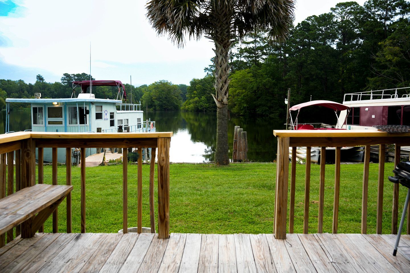 A wooden deck with a bench, a small boat house, and a large tree.