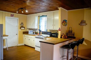 A kitchen with white cabinets, a stove, a microwave, and a sink. There is a wooden ceiling and a door marked 'EXIT'.