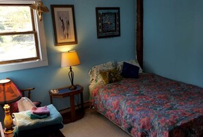 Ein Schlafzimmer mit einem Bett, einem Nachttisch, einer Lampe, einem Fenster und zwei gerahmten Bildern an der Wand.