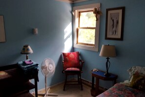 Ein Zimmer mit Fenster, Stuhl, Ventilator und Lampe.