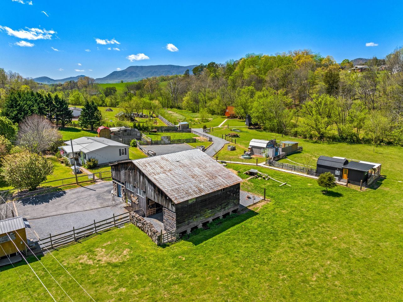 Vista aérea de uma propriedade rural com várias construções, incluindo um celeiro grande, estruturas menores e uma área cercada.