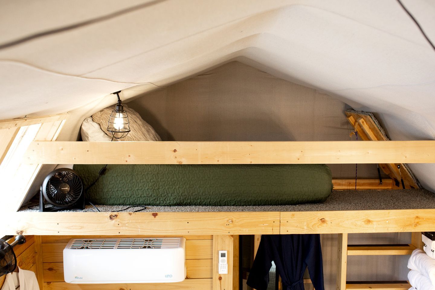 A loft-style room with a bunk bed, a heater, a fan, and a small table with a lamp.