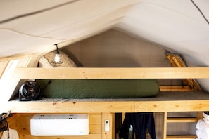 A loft-style room with a bunk bed, a heater, a fan, and a small table with a lamp.