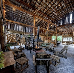 Un intérieur rustique avec une cheminée, des meubles en bois et un plafond haut avec des poutres apparentes.