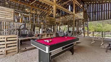 A pool table in a rustic wooden room with a high ceiling and exposed beams.