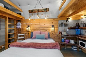 Un dormitorio acogedor con cabecera de madera, cama con ropa de cama rosa y azul, una silla blanca y un armario de madera.