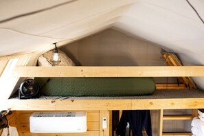 Una habitación tipo loft con literas, un calentador, un ventilador y una mesita con lámpara.