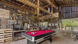 A pool table in a rustic wooden room with a high ceiling and exposed beams.