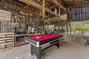 Une table de billard dans une pièce rustique en bois, dotée d’un plafond haut et de poutres apparentes.