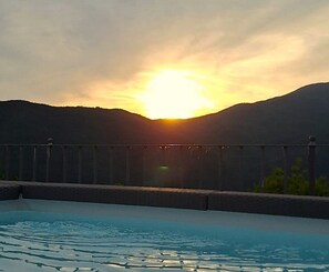 Une piscine avec vue sur le coucher de soleil, une clôture et une montagne en arrière-plan.