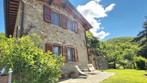 Ein Steinhaus mit Holzhörnern, einer Terrasse mit Stühlen und einem üppigen Grünpflanzen-Garten.