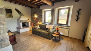 Ein gemütliches Wohnzimmer mit Kamin, Steinwänden, einem grünen Sofa und einer Holzbalkendecke.