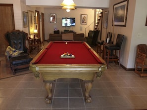 Ein Billardtisch in einem Raum mit Fernseher, Sesseln und gerahmten Bildern an den Wänden.