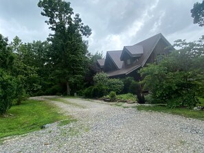 A house with a gravel driveway, surrounded by greenery and trees.