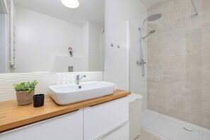 Ein modernes Badezimmer mit einem weißen Waschbecken, einer Holzauskleidung und einer Glasdusche.