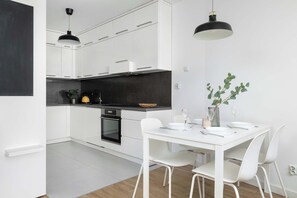 A modern kitchen with white cabinets, a black countertop, and a dining area with a white table and chairs. - Modern Apartment with Parking | Balcony | Workspace (Kraków)