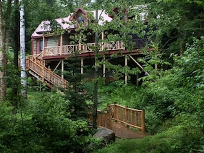 A cabin with a wooden deck and staircase, surrounded by dense forest. - Elegantly Rustic Cabin on Secluded Island near Lake Placid on Saranac Lake, New York (Saranac Lake)