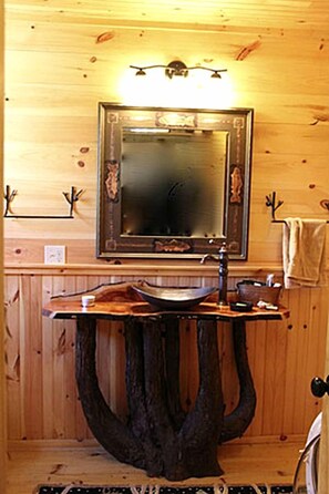 A wooden cabin interior with a wooden-framed mirror, a sink with a unique tree stump base, and a towel hanging on a rack. - Elegantly Rustic Cabin on Secluded Island near Lake Placid on Saranac Lake, New York (Saranac Lake)